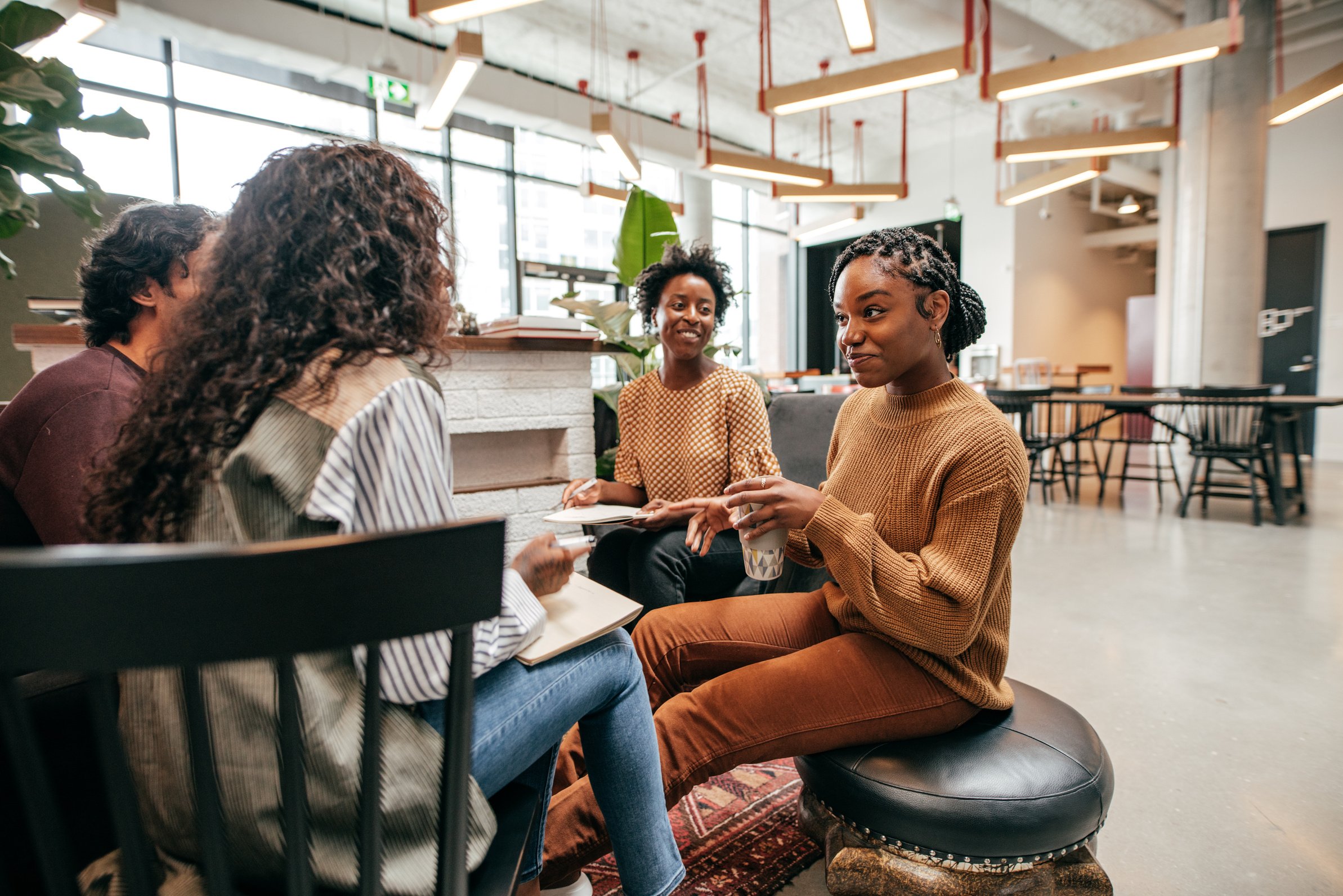 a group of women sitting around a table in an office, representing collaboration and relationship-building